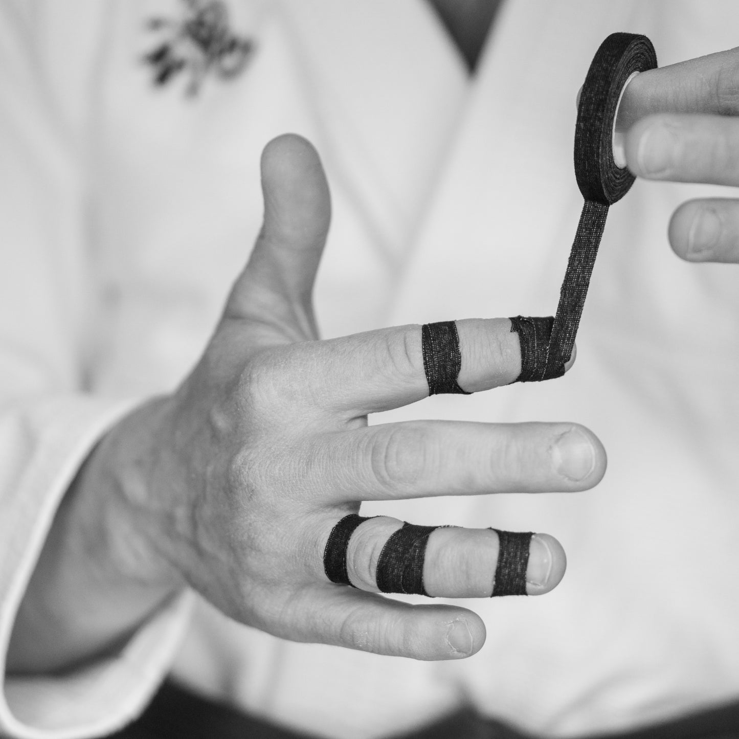 Jiu jitsu athlete wrapping black BJJ finger tape around fingers for joint support and grip protection.